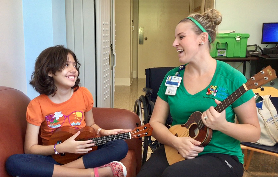 Ukulele Kids Club president Stephanie Epstein plays ukulele with a child in a hospital room