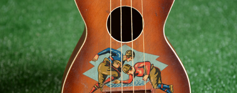 The football-themed “Touchdown” ukulele from the 1920s with a decal just above the bridge depicting a pair of rival college players wearing hardened leather helmets and padded uniforms